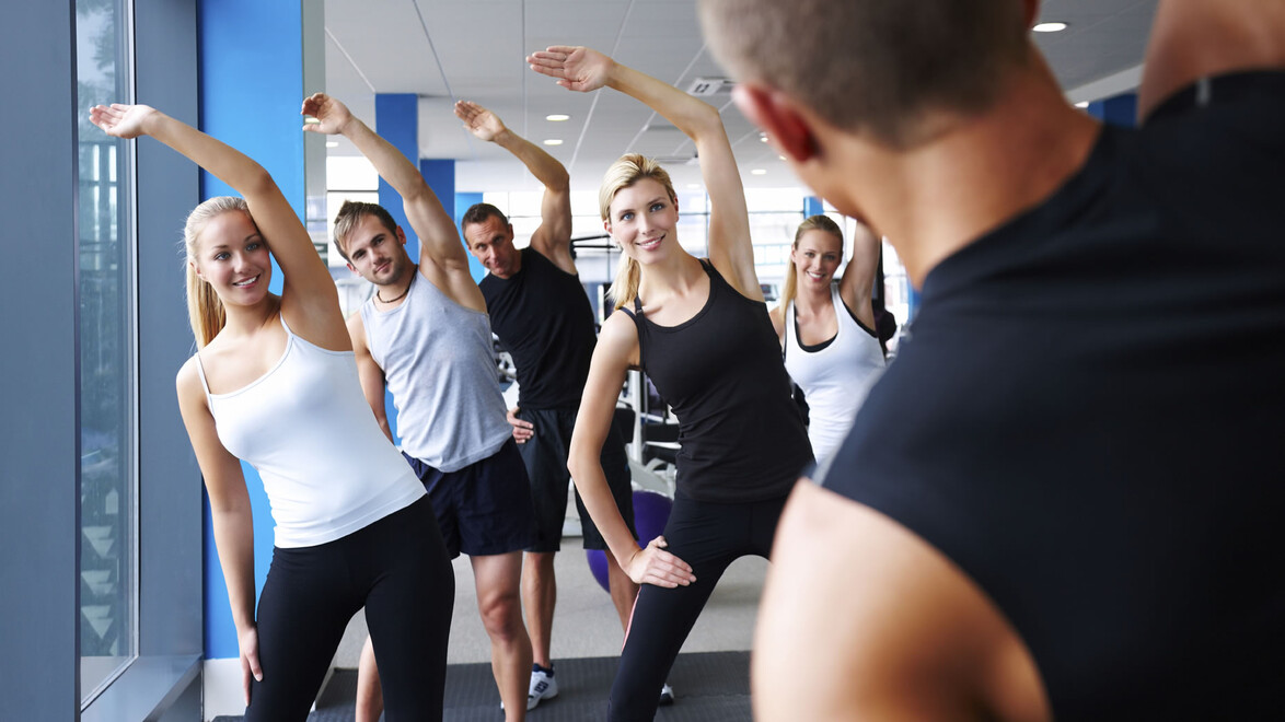 Gruppe junger Erwachsener beim Aufwärmtraining in einem hellen Fitnessraum / Group of young adults warming up in a bright fitness room