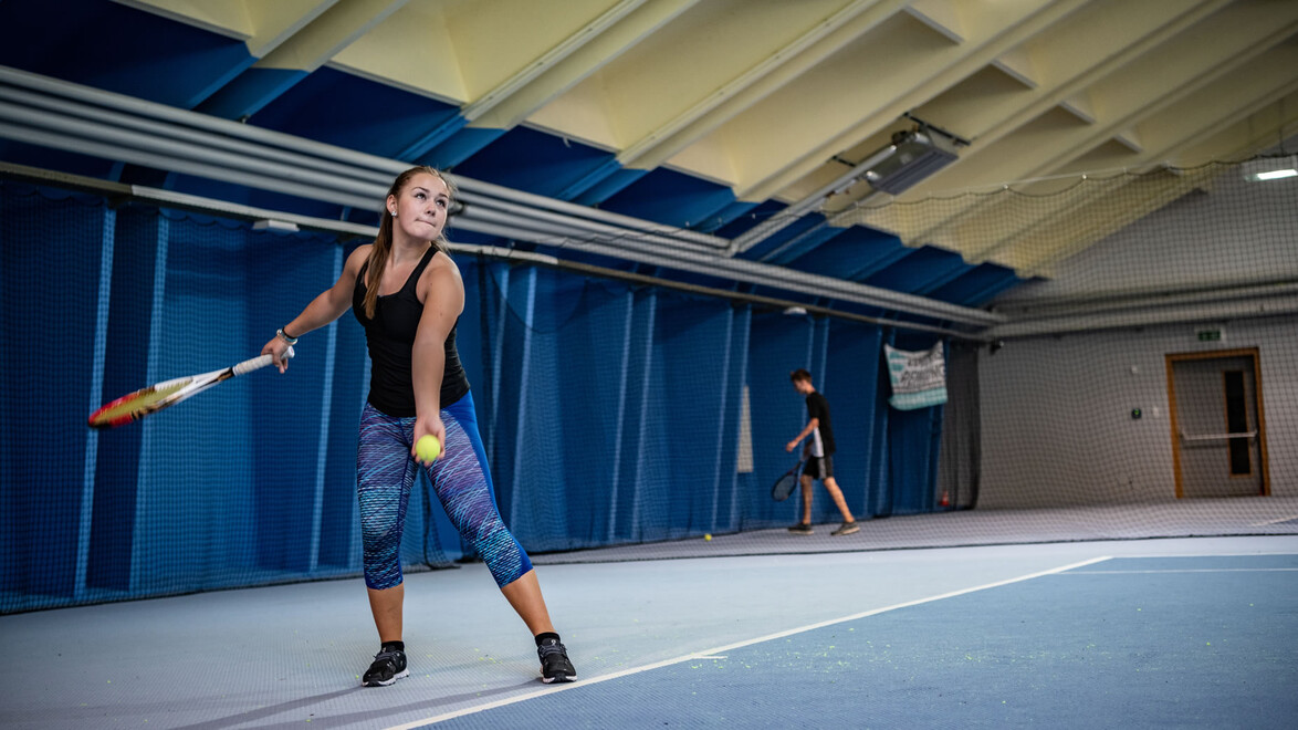 Frau beim Aufschlag in der Tennishalle / Woman serving in indoor tennis hall