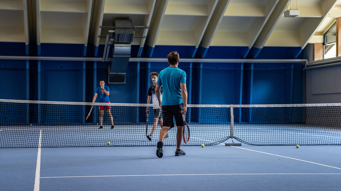 Zwei Personen beim Tennis-Doppelspiel in der Halle / Two people playing doubles in an indoor tennis court