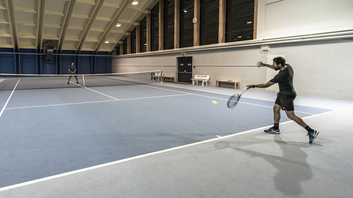Mann beim Tennisspiel in heller Halle mit Netz / Man playing tennis in a bright indoor hall with net