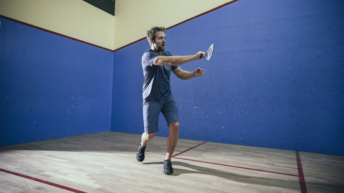 Mann beim Squashspiel in blauer Halle / Man playing squash in a blue-walled indoor court