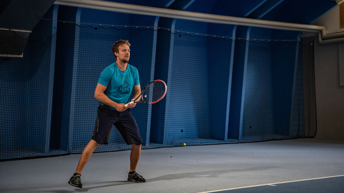 Tennisspieler in blauer Halle in Spielhaltung / Tennis player in ready position in blue indoor hall