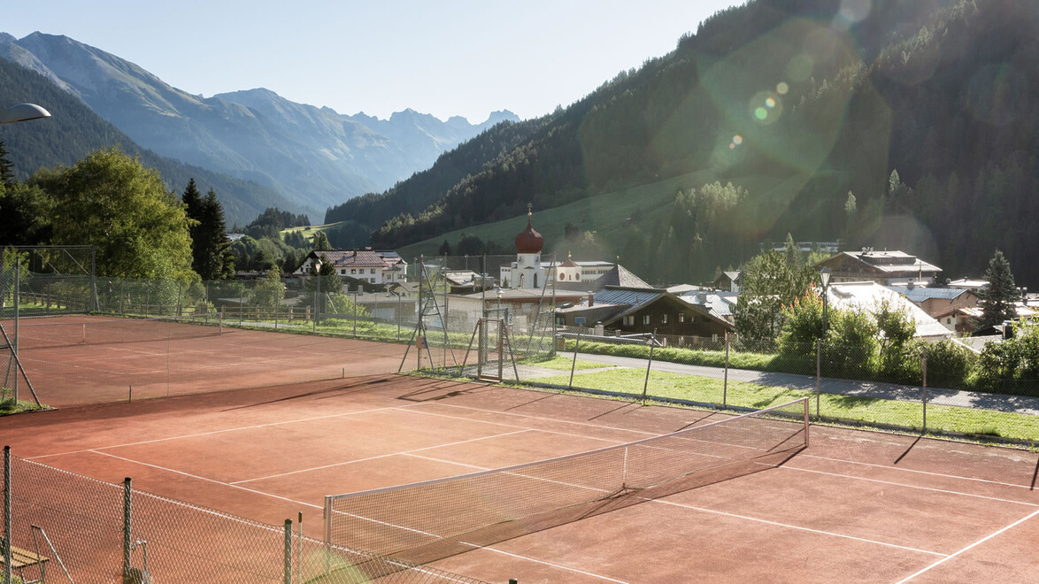 Roter Tennisplatz im Freien mit Blick auf Berge und Ort / Outdoor red clay tennis court with mountains and village view
