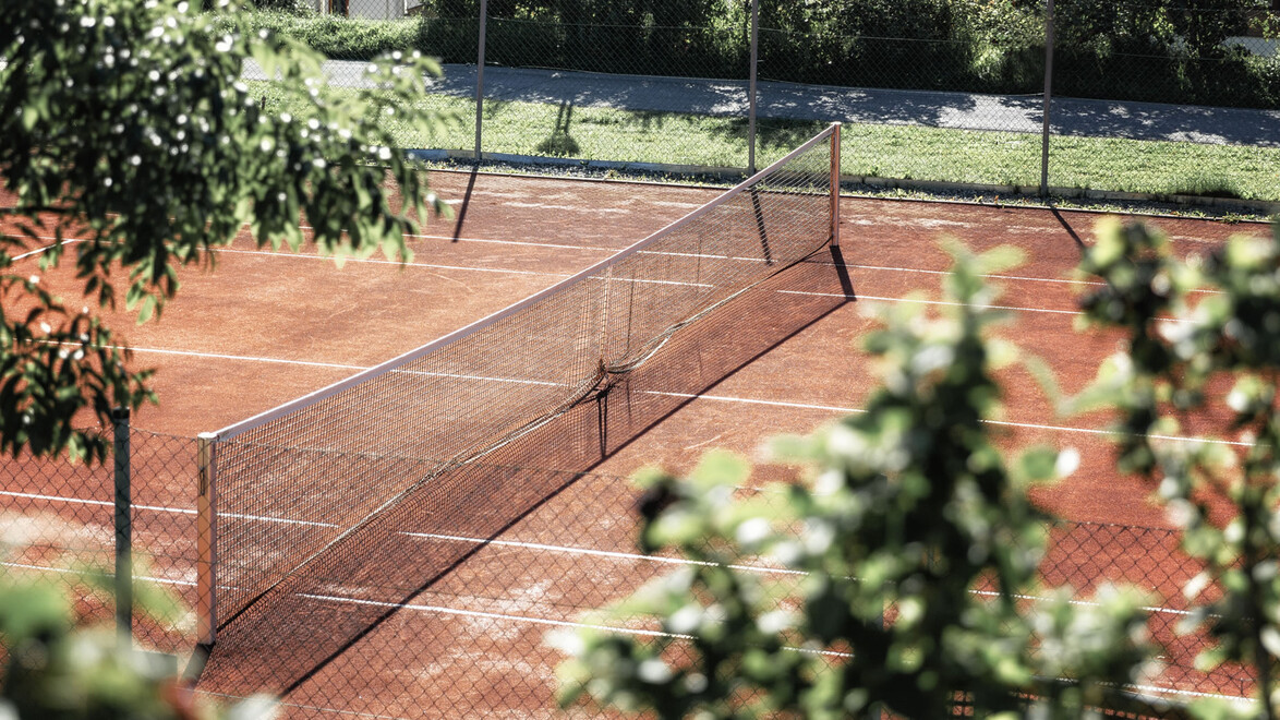 Freiluft-Tennisplatz mit Netz, umgeben von Bäumen / Outdoor clay tennis court with net, surrounded by trees