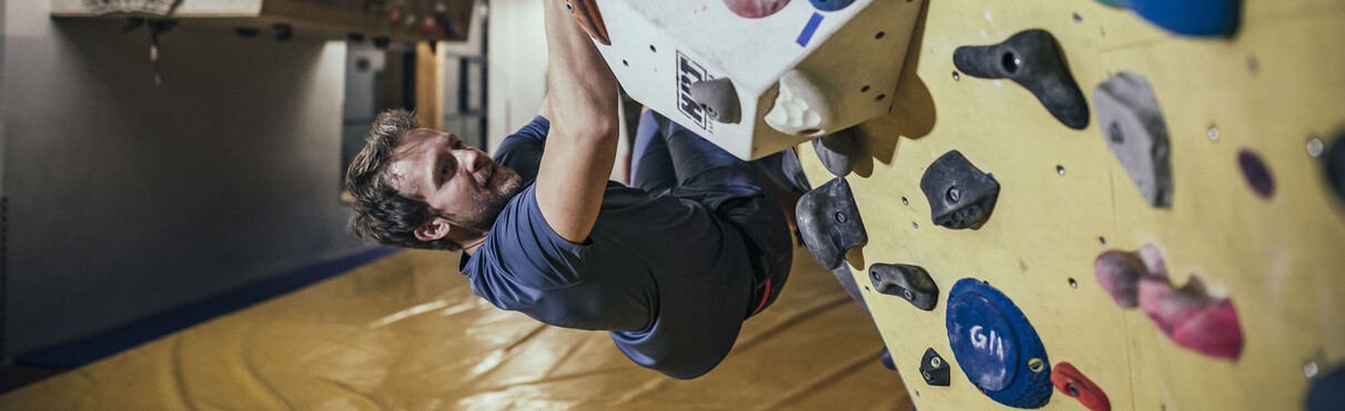 Man bouldering on an overhang wall inside a climbing gym.