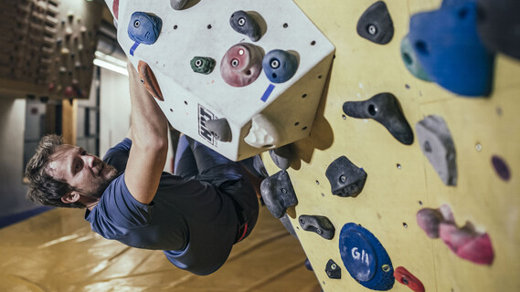 Man bouldering on an overhanging indoor climbing wall with colorful holds.