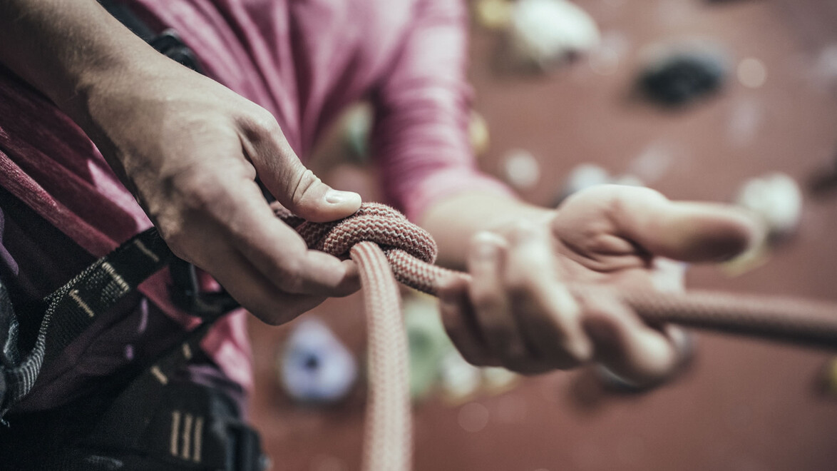 Hände beim Einbinden eines Kletterseils in den Gurt / Hands tying a climbing rope to the harness