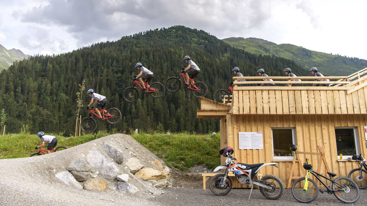 Sequenzaufnahme zeigt Sprung eines Bikers vor Hütten-Kulisse / Sequence image shows biker jump in front of hut backdrop
