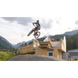 Biker springt über Erdhügel vor Holzgebäude im Bikepark / Biker jumps over dirt hill in front of wooden building at bike park