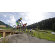 Zwei Kinder auf Mountainbikes springen gleichzeitig über Erdhügel im Bikepark / Two kids on mountain bikes jump simultaneously over a dirt hill in the bike park