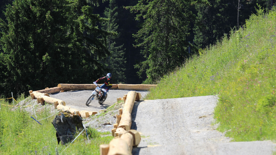 Motocross-Fahrer nimmt enge Kurve auf Waldtrail mit Holzbegrenzung / Motocross rider takes tight curve on forest trail with wooden barriers