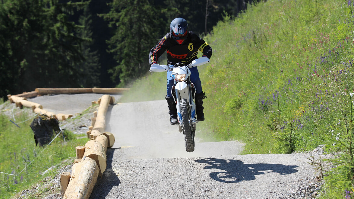 Motocross-Fahrer springt über Erhebung auf staubiger Bergstrecke / Motocross rider jumps over a bump on a dusty mountain trail