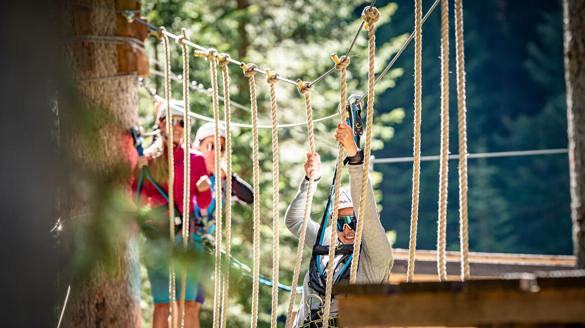 Zwei Personen auf Plattform im Wald, durch Seilnetz getrennt, Hochseilgarten-Parcours / Two people on forest platform, separated by rope net, high ropes course