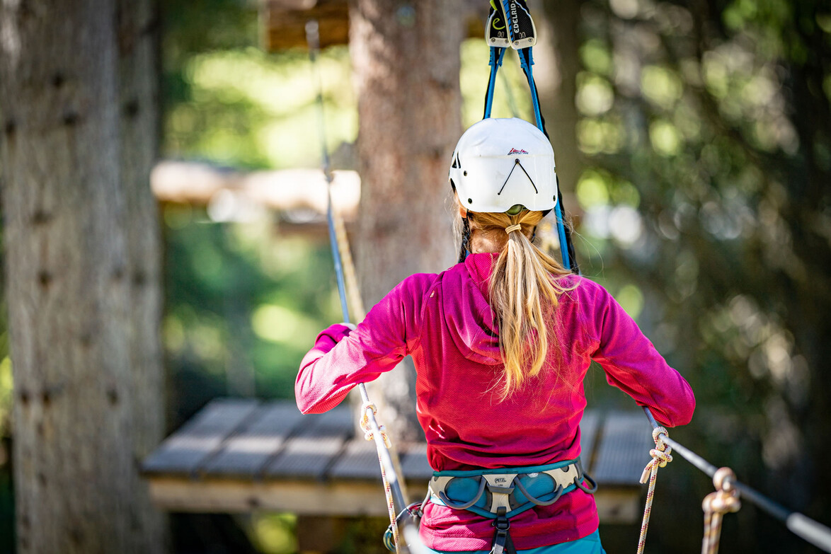 Teilnehmerin mit Helm am Hochseil, Rückenansicht, zwischen Plattform und Seil gespannt / Participant with helmet on high rope, rear view, between platform and rope tension