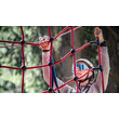 Kind mit Helm greift ein rotes Kletternetz im Hochseilgarten, konzentrierter Blick / Child with helmet grips red climbing net in high ropes course, focused expression