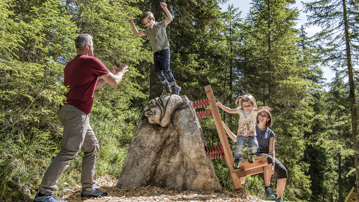 Familie spielt mit Felseninstallation und Holzbank / Family playing on rock sculpture with wooden bench