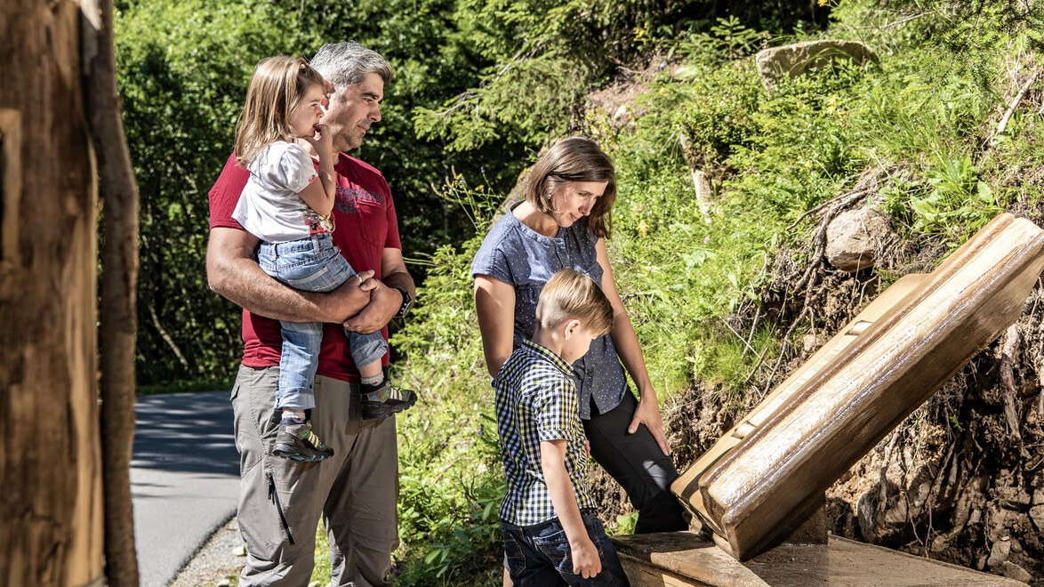 Familie betrachtet Wasserspiel aus Holzrinnen / Family explores wooden water play station