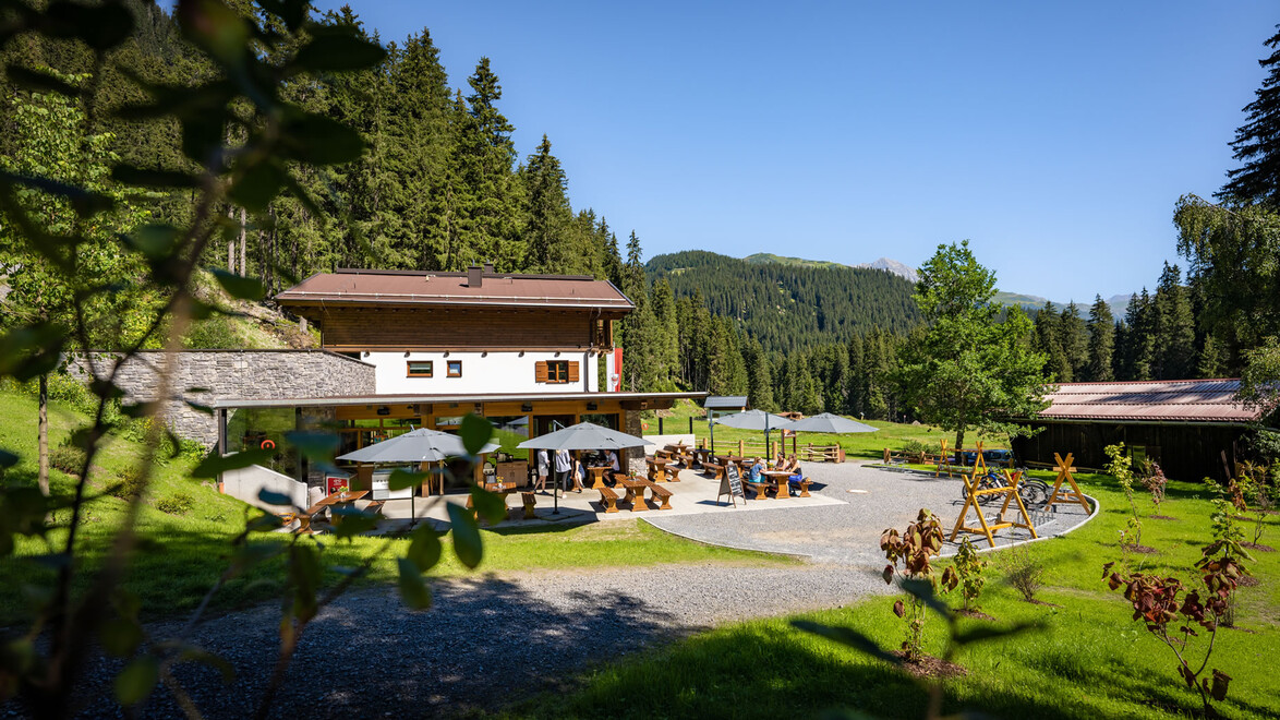 Gastgarten mit Schirmen vor traditionellem Haus im Grünen / Outdoor dining with umbrellas in front of alpine house
