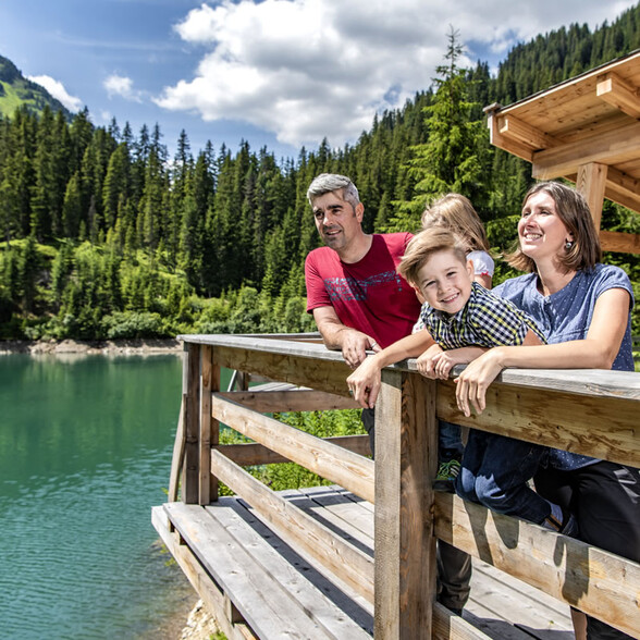 A happy family enjoys the lake view and surrounding mountains from a wooden viewing platform.