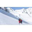 Eine Gruppe von Skitourengeher:innen durchquert eine sonnige Winterlandschaft mit weiten Schneefeldern / A group of ski tourers crosses a sunny winter landscape with wide snowfields