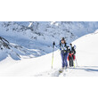 Zwei Skitourengeherinnen steigen mit Tourenski durch verschneites Gelände, im Hintergrund eine winterliche Bergkulisse / Two ski tourers ascend a snowy slope with touring skis, surrounded by alpine winter scenery