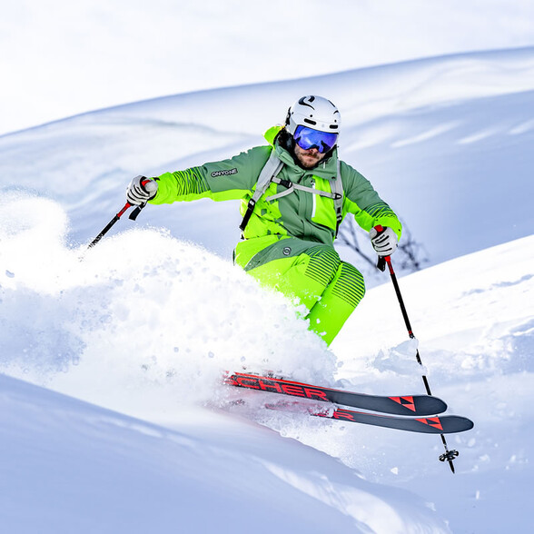 Freerider in neon green speeds through deep powder snow.