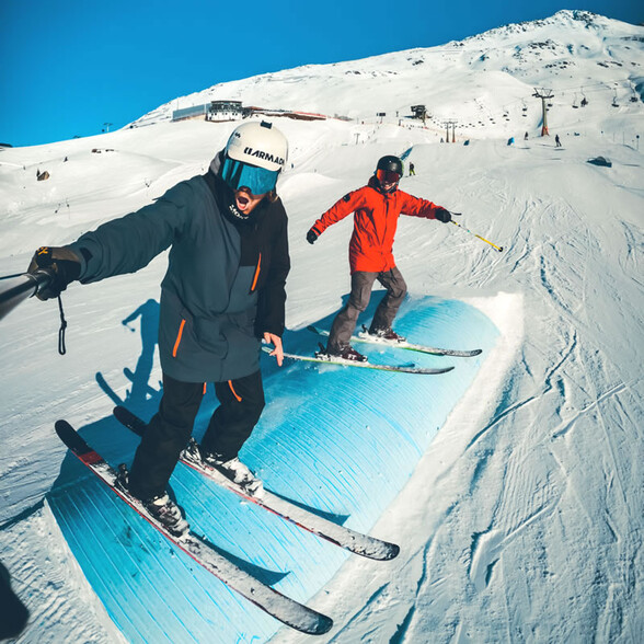Two freestyle skiers balance side by side on a snow park obstacle.