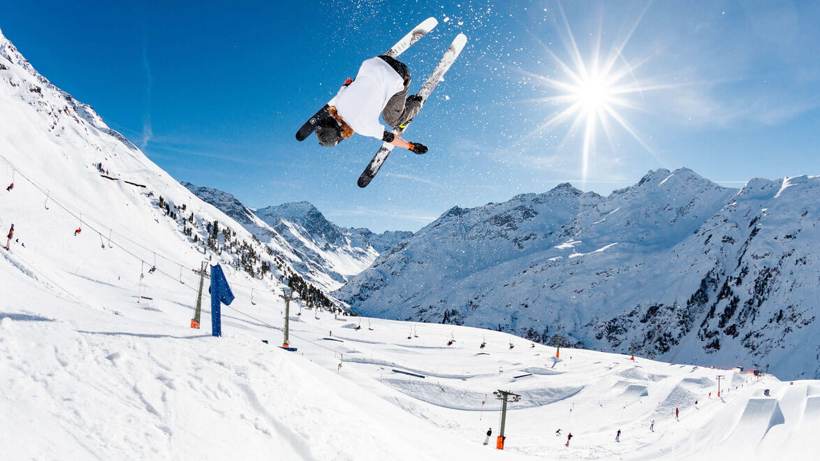 Ein Freeskier führt einen spektakulären Sprung bei strahlendem Sonnenschein im Snowpark aus / A freeskier performs a spectacular jump in the snow park under bright sunshine
