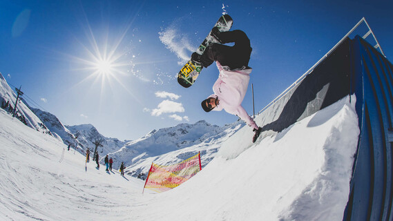 Snowboarder performs a wallride trick in the sun at the snow park.