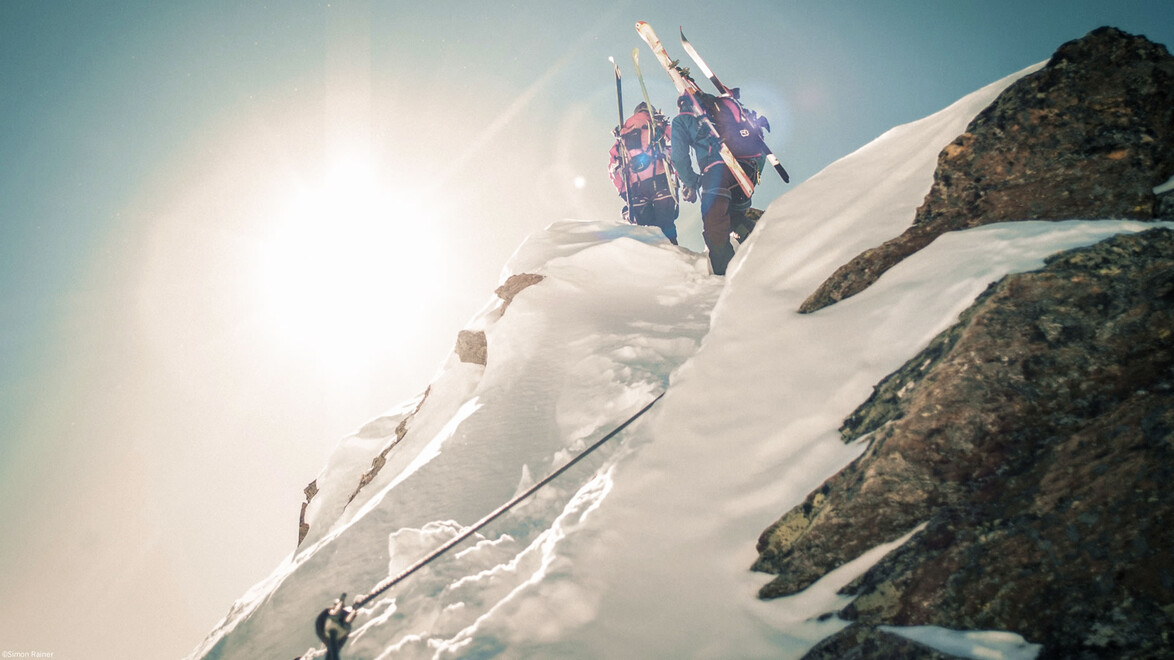 verschneiten Grat bei starker Sonneneinstrahlung auf / Four ski mountaineers with skis on backpacks ascend a narrow snowy ridge under strong sunlight