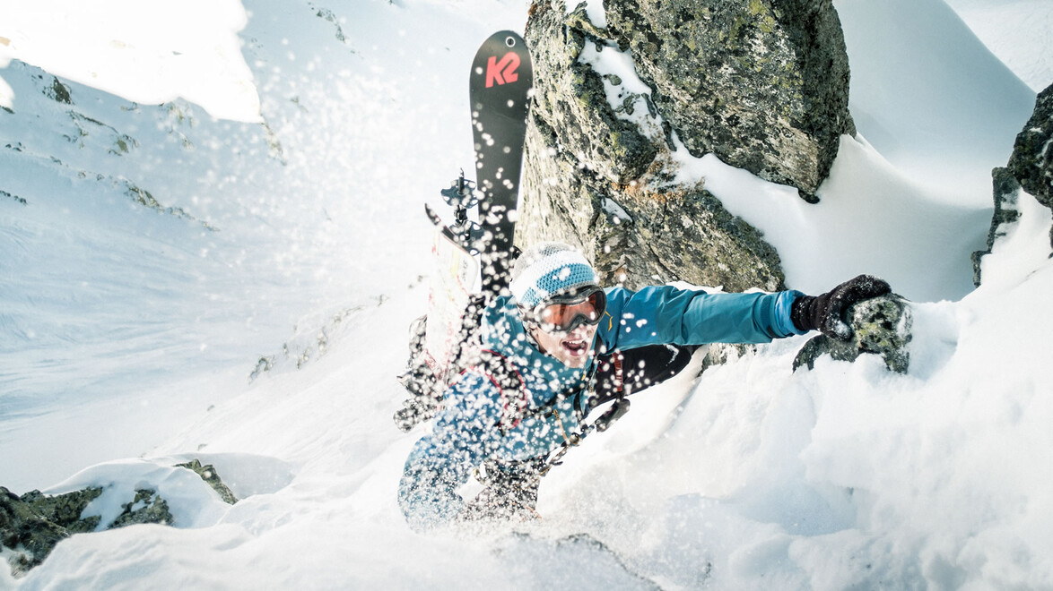Ein Skitourengeher erklimmt mit angeschnallten Skiern eine steile, verschneite Felspassage zwischen hohen Felswänden / A ski mountaineer climbs a steep snowy rock passage with skis attached, surrounded by cliffs