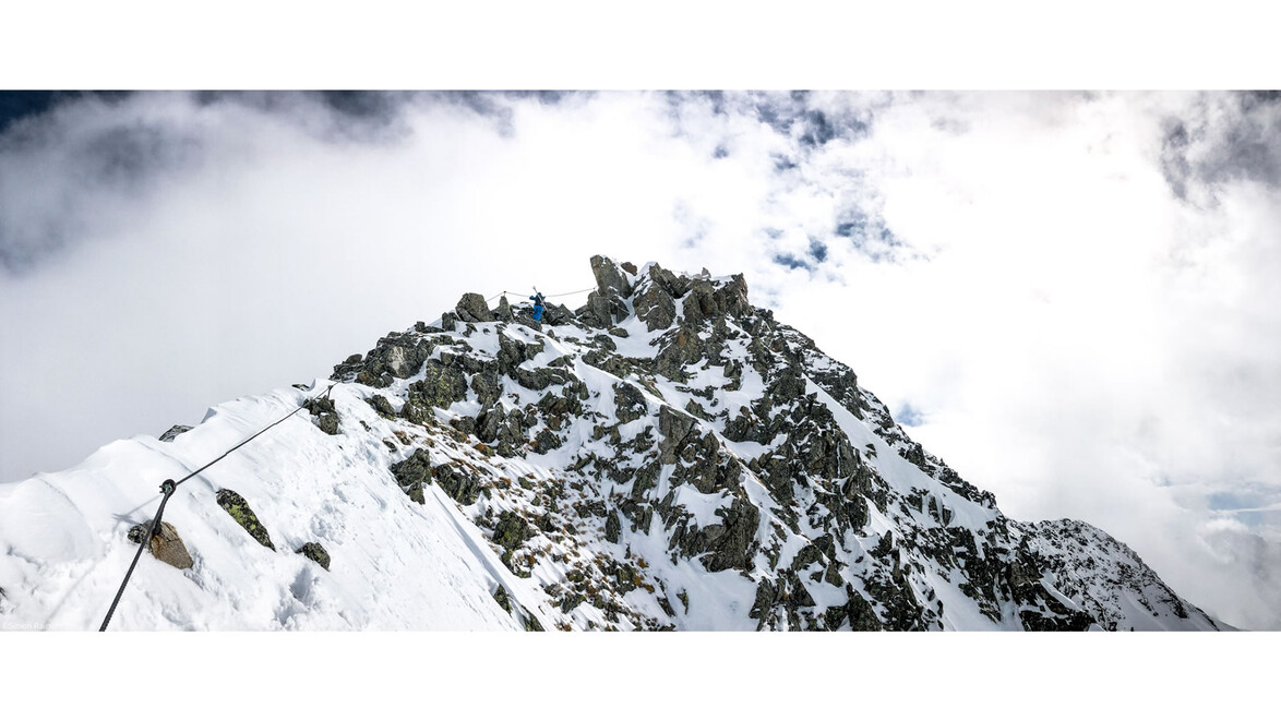 Panoramaaufnahme eines schneebedeckten Winterklettersteigs mit Seilsicherungen entlang eines felsigen Grats / Panoramic shot of a snowy winter via ferrata with rope safety lines along a rocky ridge