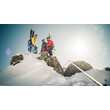 Drei Skitourengeher:innen stehen auf einem schneebedeckten Felsgrat mit atemberaubendem Ausblick und strahlender Sonne im Hintergrund / Three ski mountaineers stand on a snowy ridge with breathtaking views and bright sun in the background