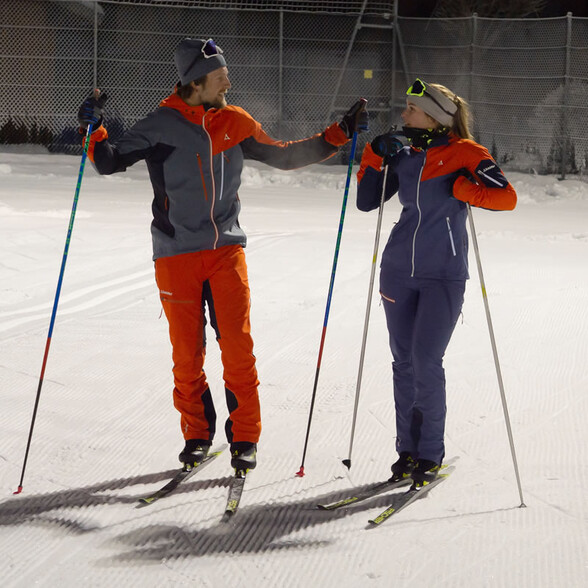 Zwei Langläufer unterhalten sich beim Nachtlanglauf auf einer beleuchteten Loipe.