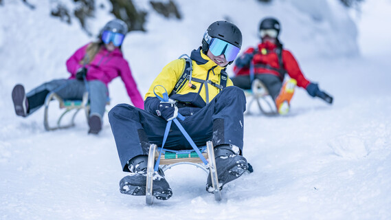 Three sledders ride downhill side by side on a snowy slope.
