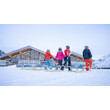 Vier Menschen mit Rodeln stehen vor einer verschneiten Berghütte / Four people with sleds stand in front of a snowy mountain hut