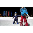 Nahaufnahme von zwei Kindern beim Eislaufen, begleitet von hellem Flutlicht und Fahnen im Hintergrund / Close-up of two kids ice skating under floodlights with flags in the background