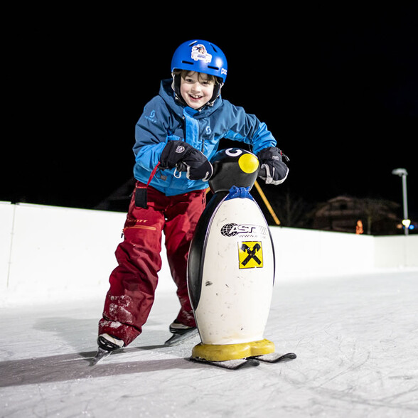 Boy skates with a penguin skating aid and laughs joyfully.