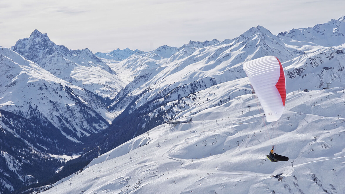 Paragleiter fliegt über eine verschneite Berglandschaft mit weitem Talblick / Paraglider flying over snowy mountain landscape with wide valley view