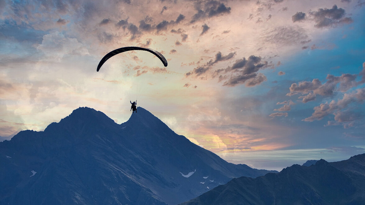 Silhouette eines Paragliders vor Sonnenuntergang über Berggipfeln / Paraglider silhouette at sunset above mountain peaks