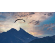 Silhouette eines Paragliders vor Sonnenuntergang über Berggipfeln / Paraglider silhouette at sunset above mountain peaks