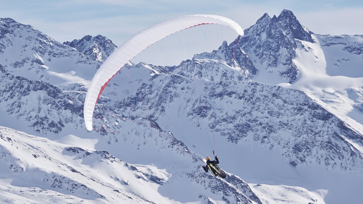 Paragleiter über schneebedeckten Gipfeln mit elegantem Bogen des Schirms / Paraglider over snow-covered peaks with elegant canopy arc
