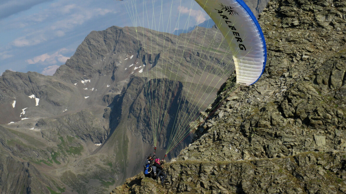 Gleitschirm startet nahe Felskante in grüner Bergwelt / Paraglider launching near rocky edge in green alpine scenery