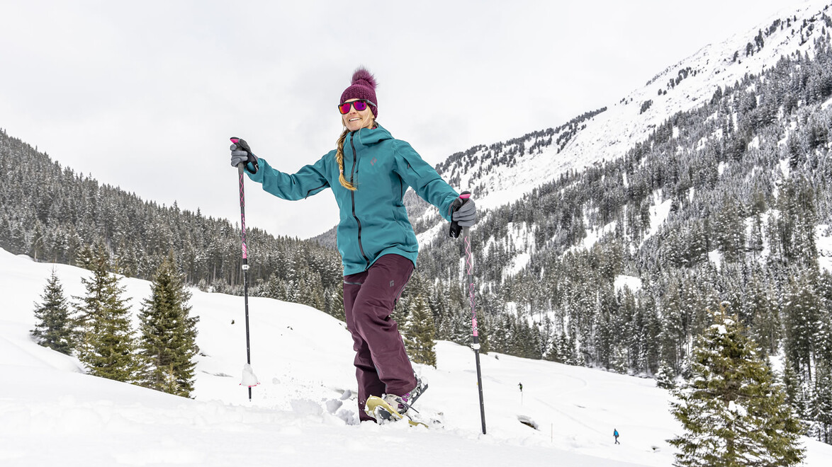 Frau genießt beim Schneeschuhwandern die Aussicht auf schneebedeckte Berge / Woman enjoys the view of snow-covered mountains while snowshoeing