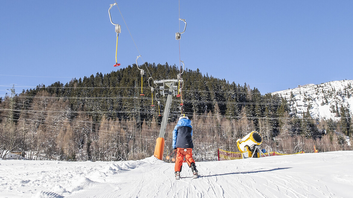 Kinderlift im Skigebiet / Children's lift in ski area Kinder ziehen sich mit Tellerlift einen Hang hinauf / Children are pulled uphill with a button lift