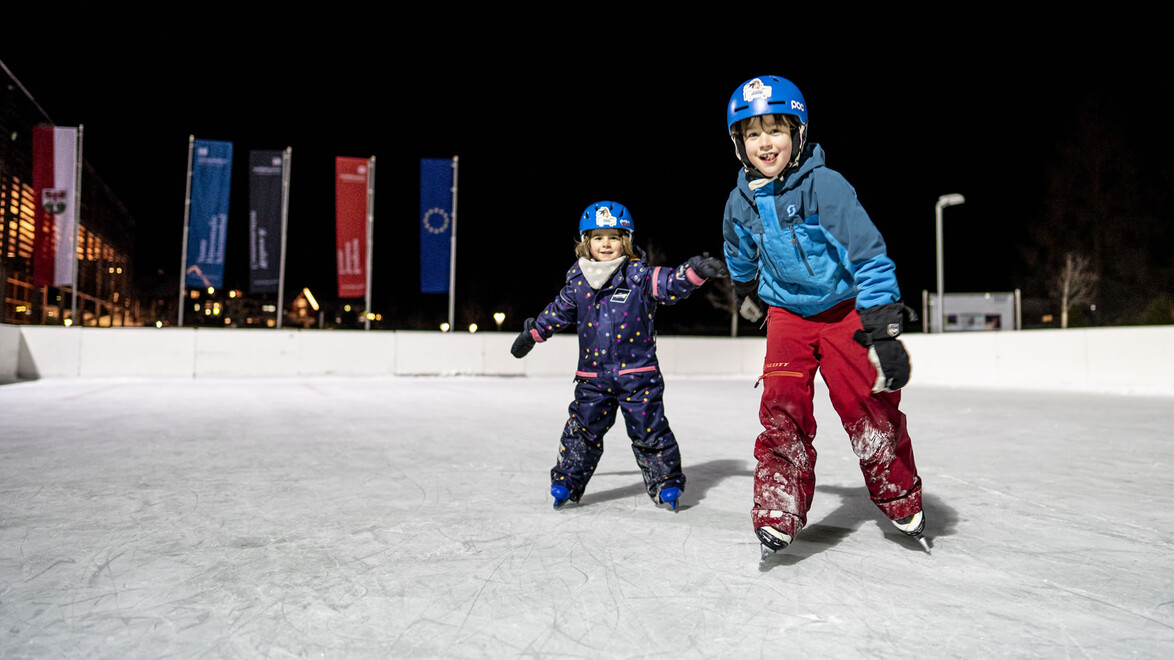 Eislaufen am Abend / Ice skating in the evening Zwei Kinder laufen am beleuchteten Eislaufplatz bei Nacht / Two children skating at night on lit ice rink
