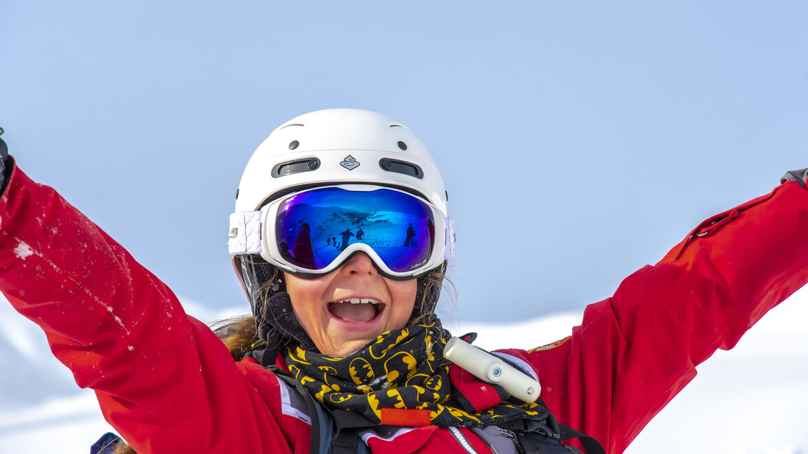 Freude beim Skifahren / Joy of skiing Lachende Skilehrerin mit erhobenen Armen vor verschneitem Hang / Smiling ski instructor with raised arms in front of snowy slope