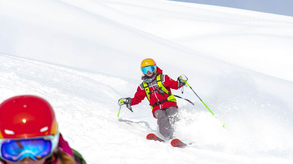 Pulverschnee Skikurs / Powder snow ski lesson Skilehrerin fährt durch frischen Pulverschnee, vorne angeschnitten ein Kind / Ski instructor rides through fresh powder snow, child partially visible in front