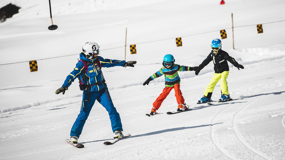 Skischule für Kinder / Ski school for kids Skilehrerin mit zwei Kindern beim Pflugfahren auf Übungshang / Ski instructor with two children snowploughing on practice slope
