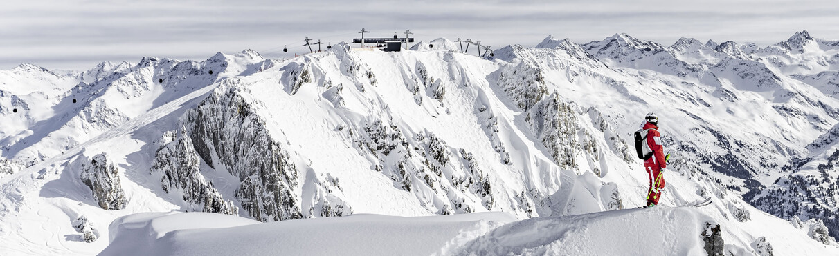 Skiër kijkt uit over het met sneeuw bedekte skigebied Valluga met bergstation en gondels.